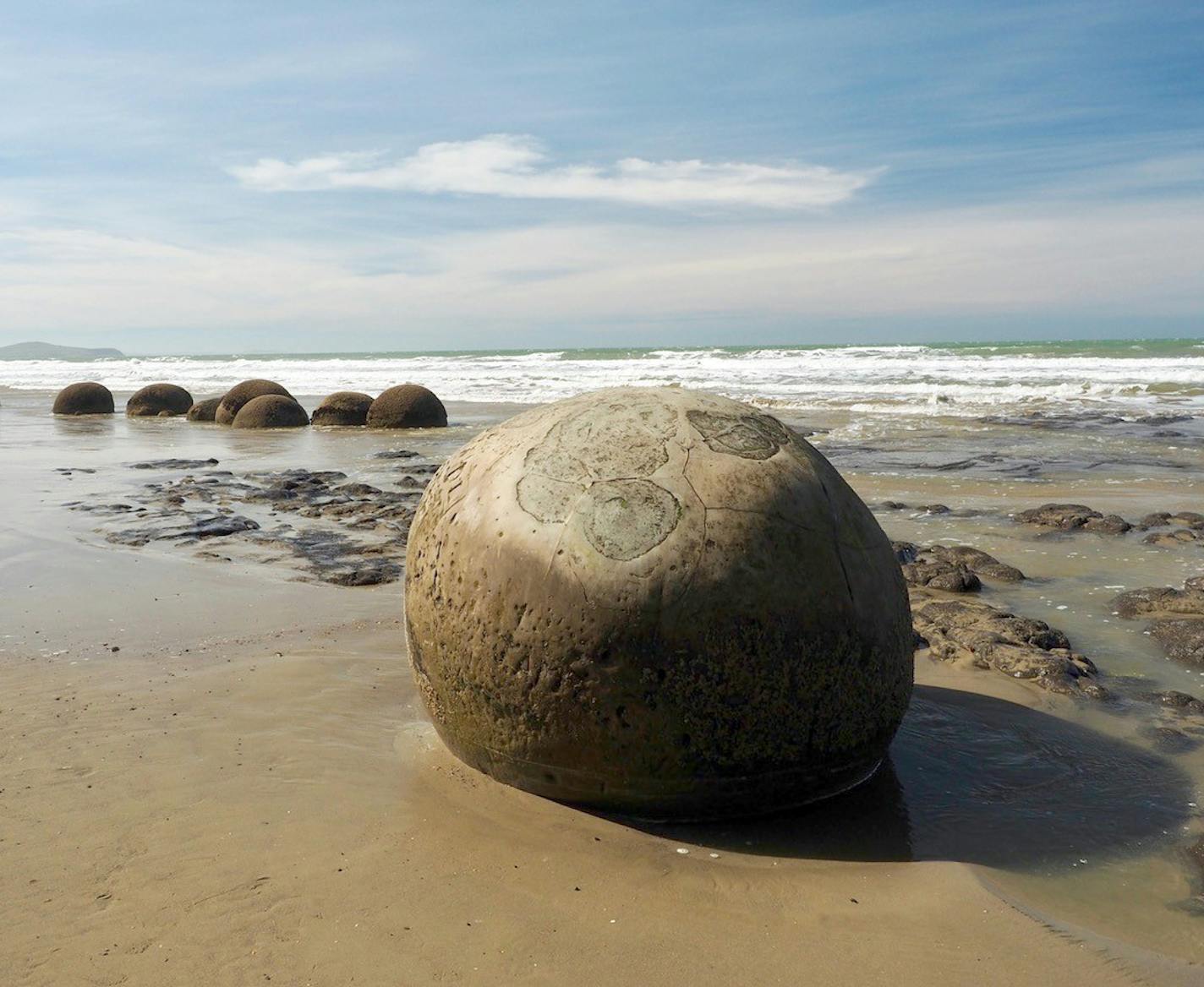 Erik Skon, Stillwater, MN Picture was taken (March, 2018) on the Otago Coast near Moeraki, New Zealand (South Island). The Moeraki Boulders are made of compressed sediment (concretions), grouped together on the beach by coastal erosion. Local Maori legend says the boulders are food baskets from the wreck of a large sailing canoe. Camera - Olympus OMD, Lens - 12 to 40 mm, 1:2.8 with circular polarizer filter, Handheld. I was struck by the mid-afternoon lighting and designs on the large boulder in