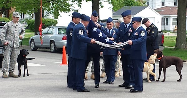 Soldiers folded an American flag flown outside of Stacy Dvorak's funeral, while others with dogs they received from Dvorak under her Operation Puppies