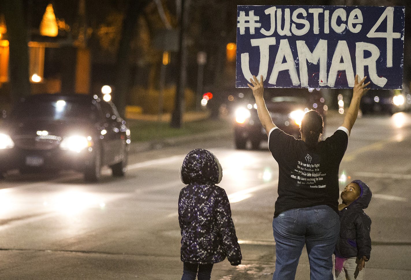 Pastor Jayme Ali, standing with her two daughters Cedreeana Day, 7, and Amirianna Day, 4, holds up a sign on Plymouth Avenue after the march returned to Jamar Clark's memorial site. ] (Leila Navidi/Star Tribune) leila.navidi@startribune.com BACKGROUND INFORMATION: Wednesday, March 30, 2016. Tensions mount in Minneapolis following the announcement that there will be no charges against Minneapolis police officers in the shooting death of Jamar Clark. ORG XMIT: MIN1603302234150932