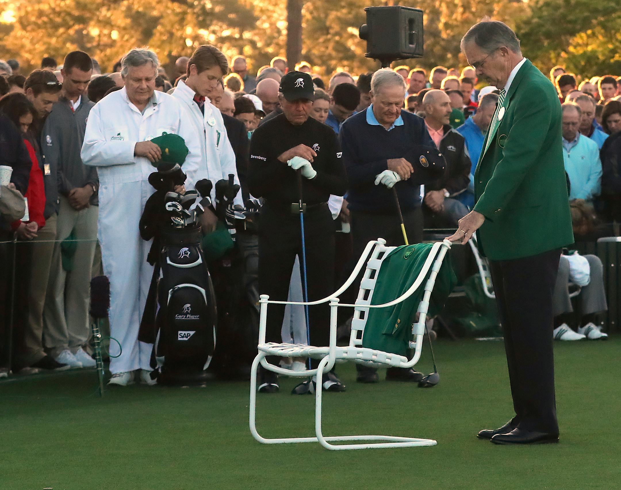 Augusta National Chairman Billy Payne, right, leads a moment of silence for Arnold Palmer, his green jacket placed in his empty chair, before Gary Player, center, and Jack Nicklaus, second from right, tee off during the honorary start of the Masters golf tournament at Augusta National Golf Club in Augusta, Ga., Thursday, April 6, 2017. (Curtis Compton/Atlanta Journal-Constitution via AP)