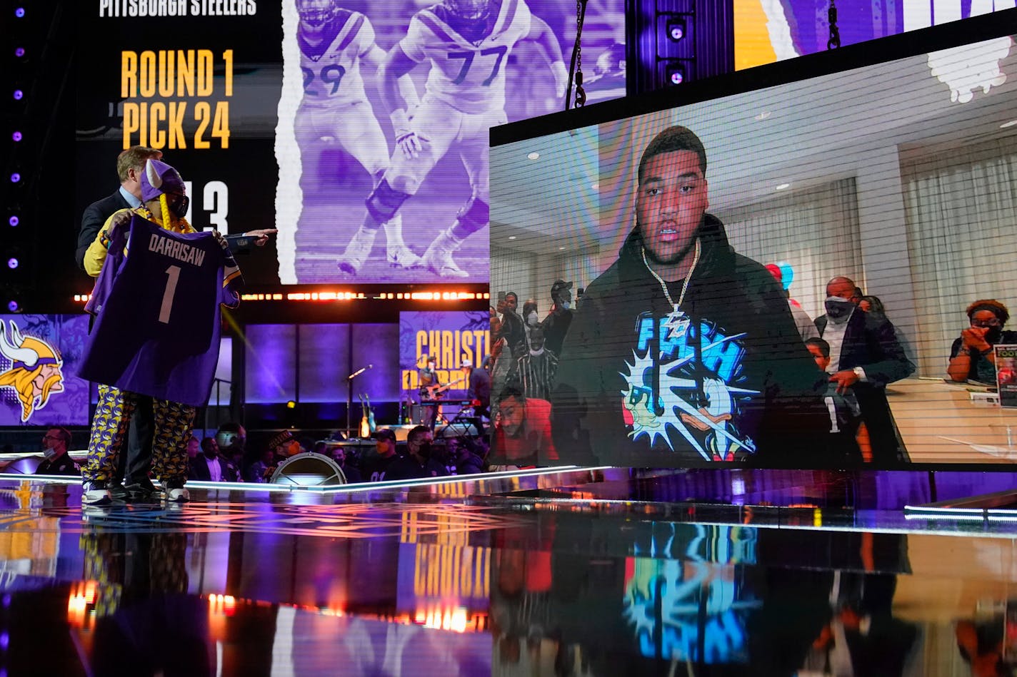 A Minnesota Vikings fan, left, holds a team jersey as an image of offensive lineman Christian Darrisaw is shown on stage after Darrisaw was chosen with the team with the 23rd pick in the first round of the NFL football draft, Thursday, April 29, 2021, in Cleveland. (AP Photo/Tony Dejak)