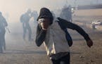 FILE - In this Nov. 25, 2018 file photo, a migrant runs from tear gas launched by U.S. agents, amid members of the press covering the Mexico-U.S. bord