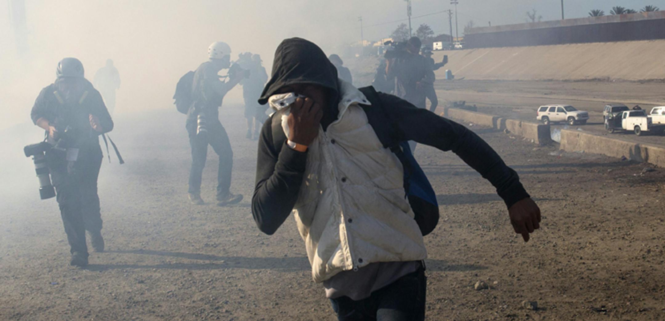 FILE - In this Nov. 25, 2018 file photo, a migrant runs from tear gas launched by U.S. agents, amid members of the press covering the Mexico-U.S. border, after a group of migrants got past Mexican police at the Chaparral crossing in Tijuana, Mexico. A San Diego TV station says the U.S. government ran an operation to screen journalists, activists and others while investigating last year's migrant caravan from Mexico. KNSD-TV says documents leaked by a Homeland Security source show a January datab