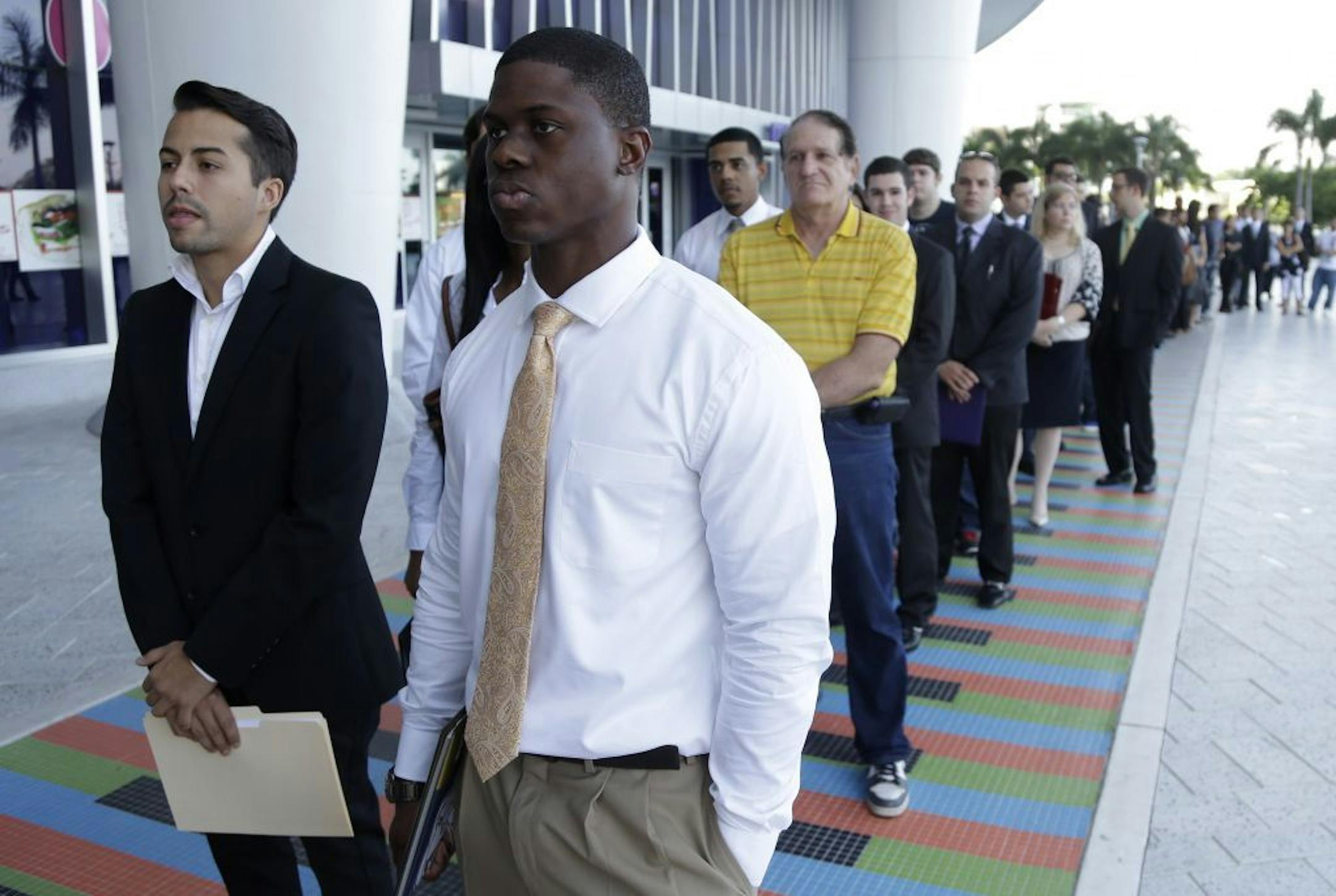 FILE - In this Wednesday, Oct. 23, 2013, file photo, Luis Mendez, 23, left, a student at Miami Dade College, left, and Maurice Mike, 23, a student at Florida International University, wait in line at a job fair held by the Miami Marlins, at Marlins Park in Miami. The job market for new college graduates is brightening but remains weaker than before the Great Recession began.