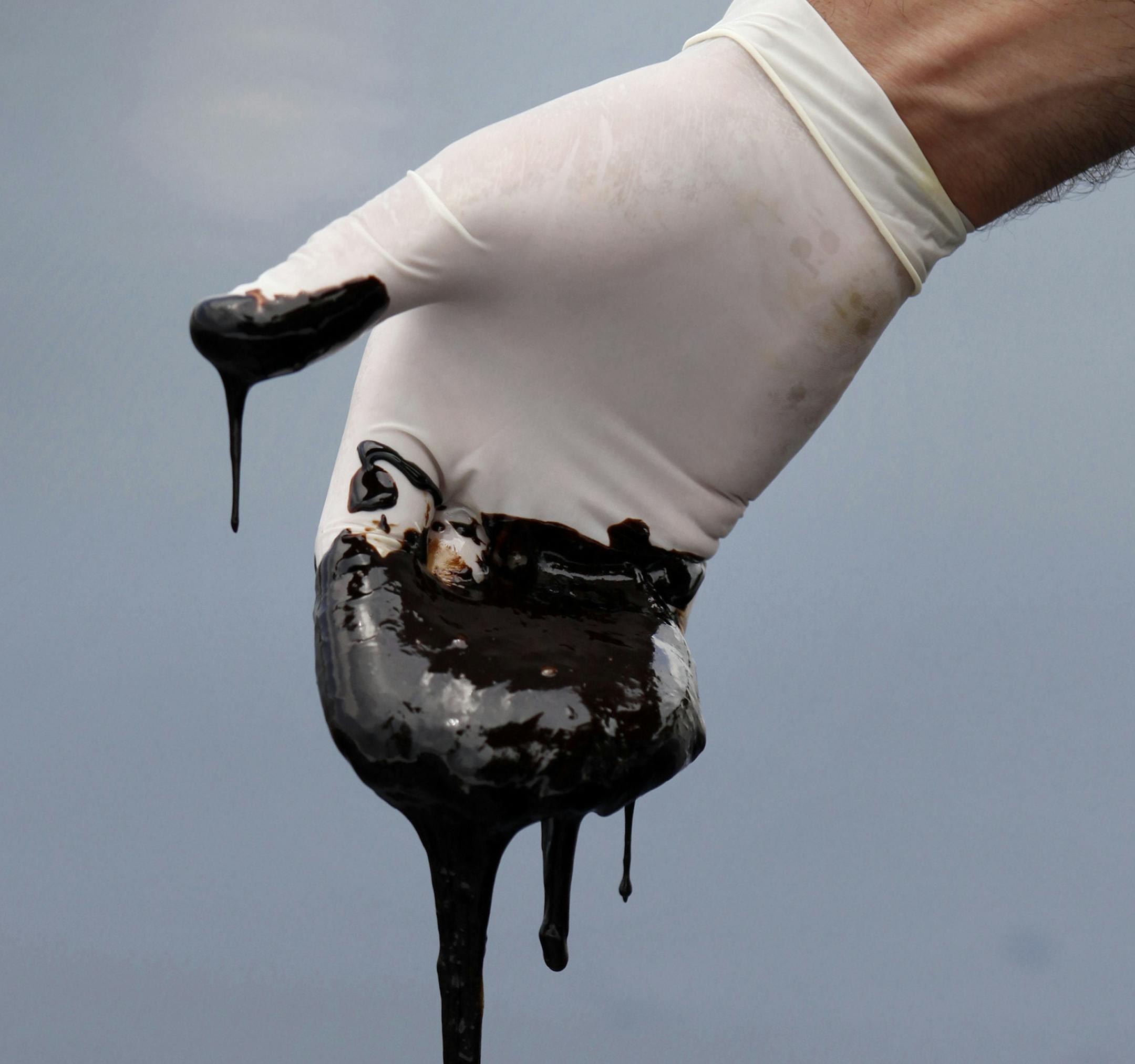 FILE - In this June 15, 2010 file photo by Gerald Herbert, a member of Louisiana Gov. Bobby Jindal's staff wearing a glove reaches into the thick oil on the surface of the northern regions of Barataria Bay in Plaquemines Parish, La. With the well still gushing, BP and the various government agencies involved were jousting over just how much oil was leaking and how much had reached shore. Journalists routinely ran into resistance from cleanup contractors telling them to stay away from oiled areas