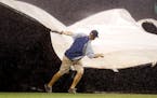 A Minnesota Twins grounds crew worker pulls the wind-blown tarp over the infield during a rain delay in the third inning of a baseball game against th