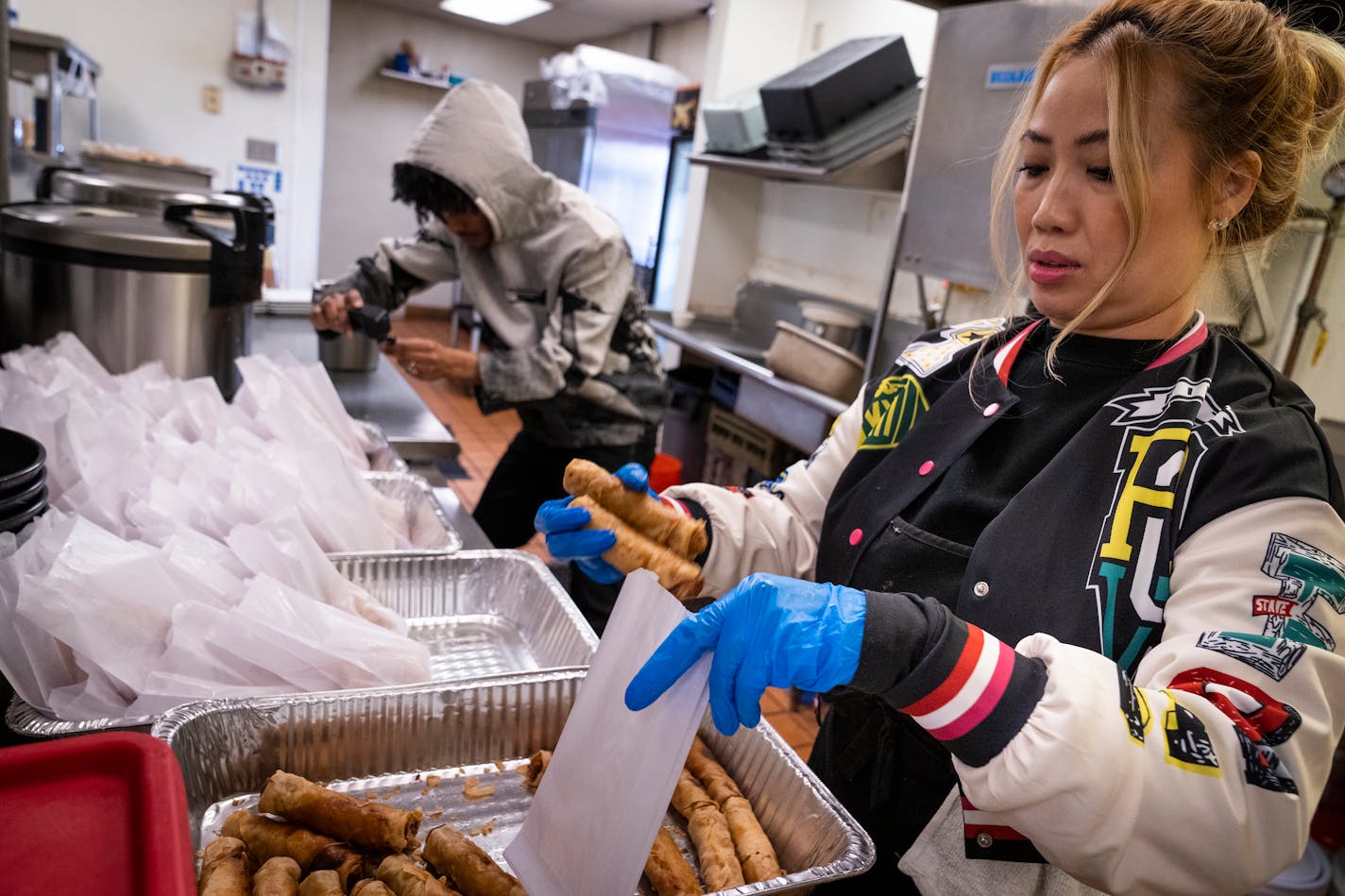 Esrom Negash, left, films while King's Thai Cuisine owner Savanh Sihanantharath, right, makes a large batch of egg rolls for TikTok creator Josh Liljenquist to pass out to the homeless at her restaurant in Fridley, Minn. Thursday, Jan. 11, 2024. Sihanantharath gave Liljenquist 120 egg rolls for free and cash to pass out to the homeless. ] LEILA NAVIDI • leila.navidi@startribune.com