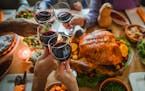 Group of unrecognizable people toasting with wine during Thanksgiving dinner at dining table.
