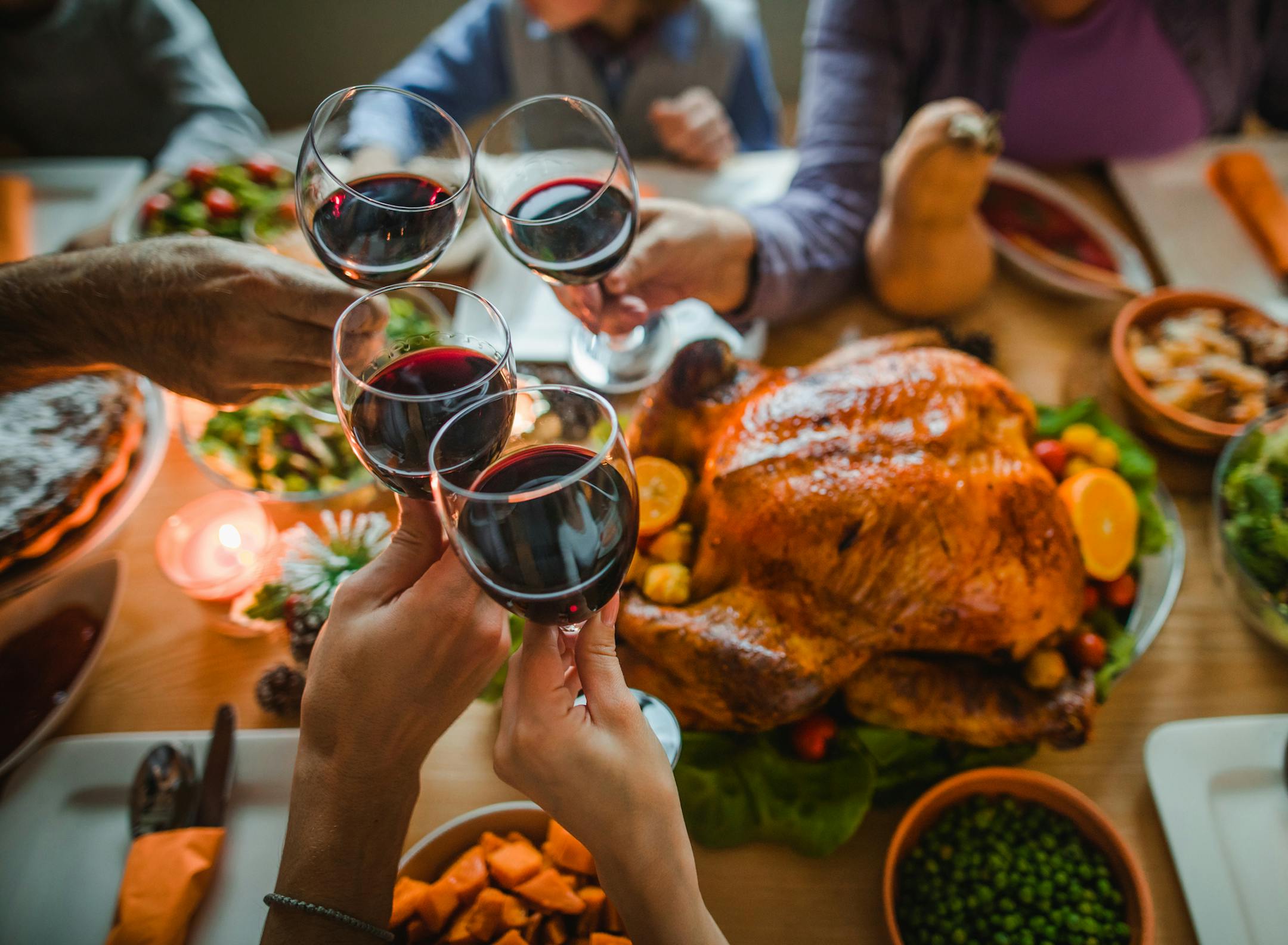 Group of unrecognizable people toasting with wine during Thanksgiving dinner at dining table.