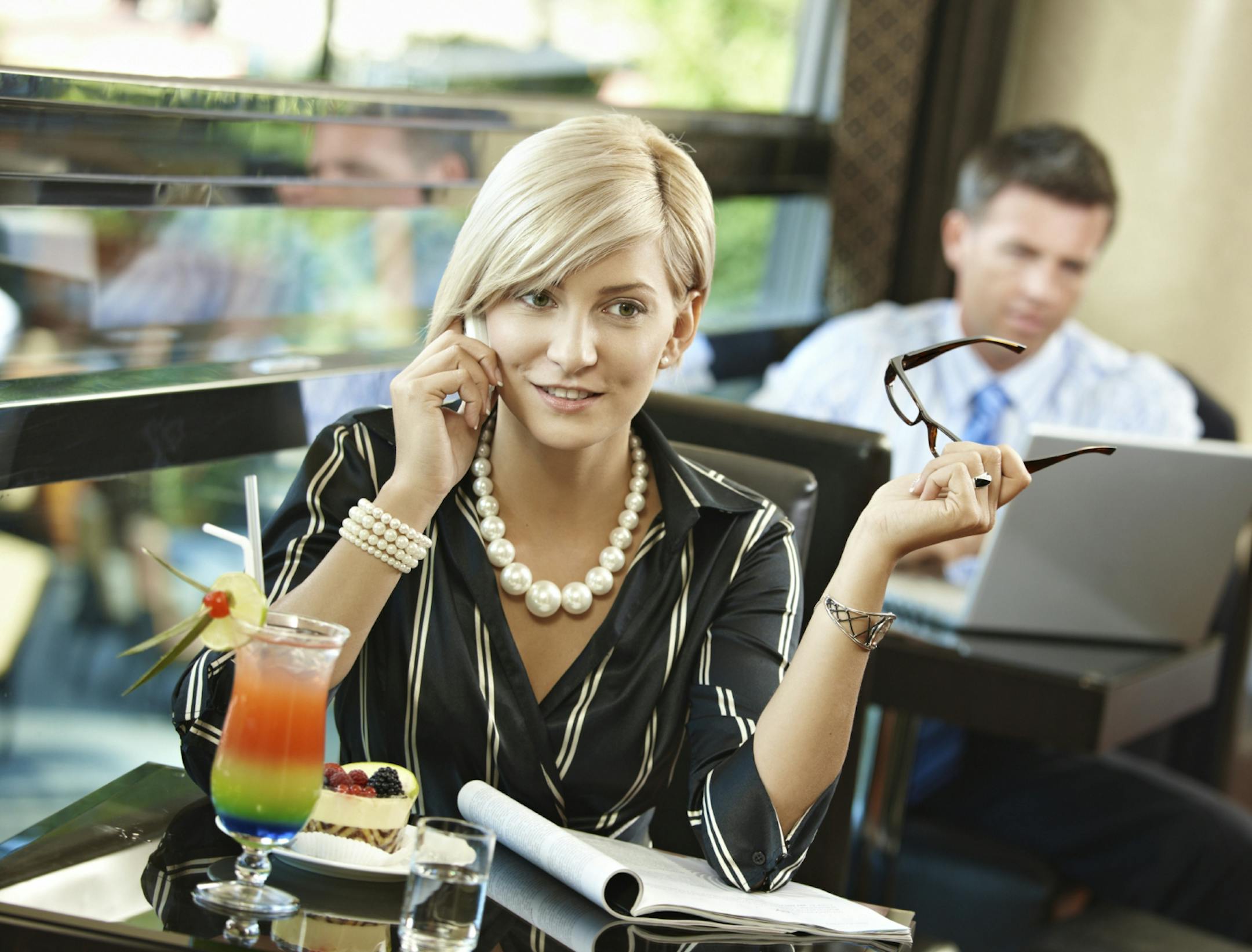 Mid-adult woman sitting at table in cafe, talking on mobile phone, reading magazine. Istock.com