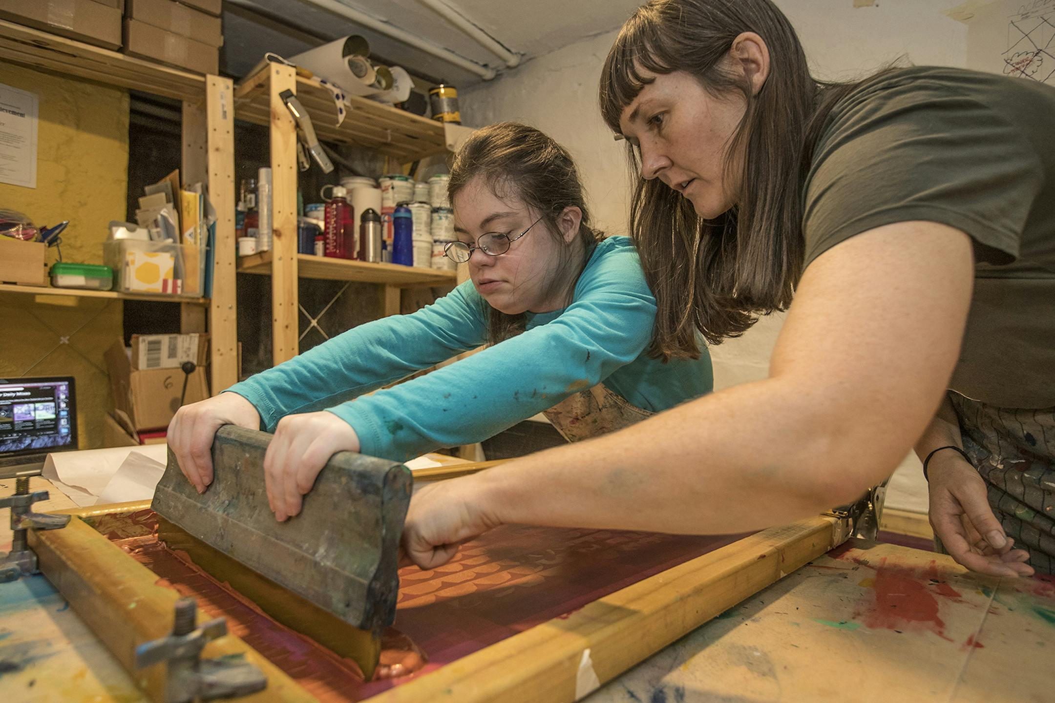 Julia Tyler, left, distributes the paint through the silk screen as her job coach, Liv Helgesen, right, makes sure the paint is distributed evenly as they work on placemants for Julia's company, Happy Dance Designs. (Michael Bryant/Philadelphia Inquirer/TNS) ORG XMIT: 1540254 ORG XMIT: MIN2001140333151159