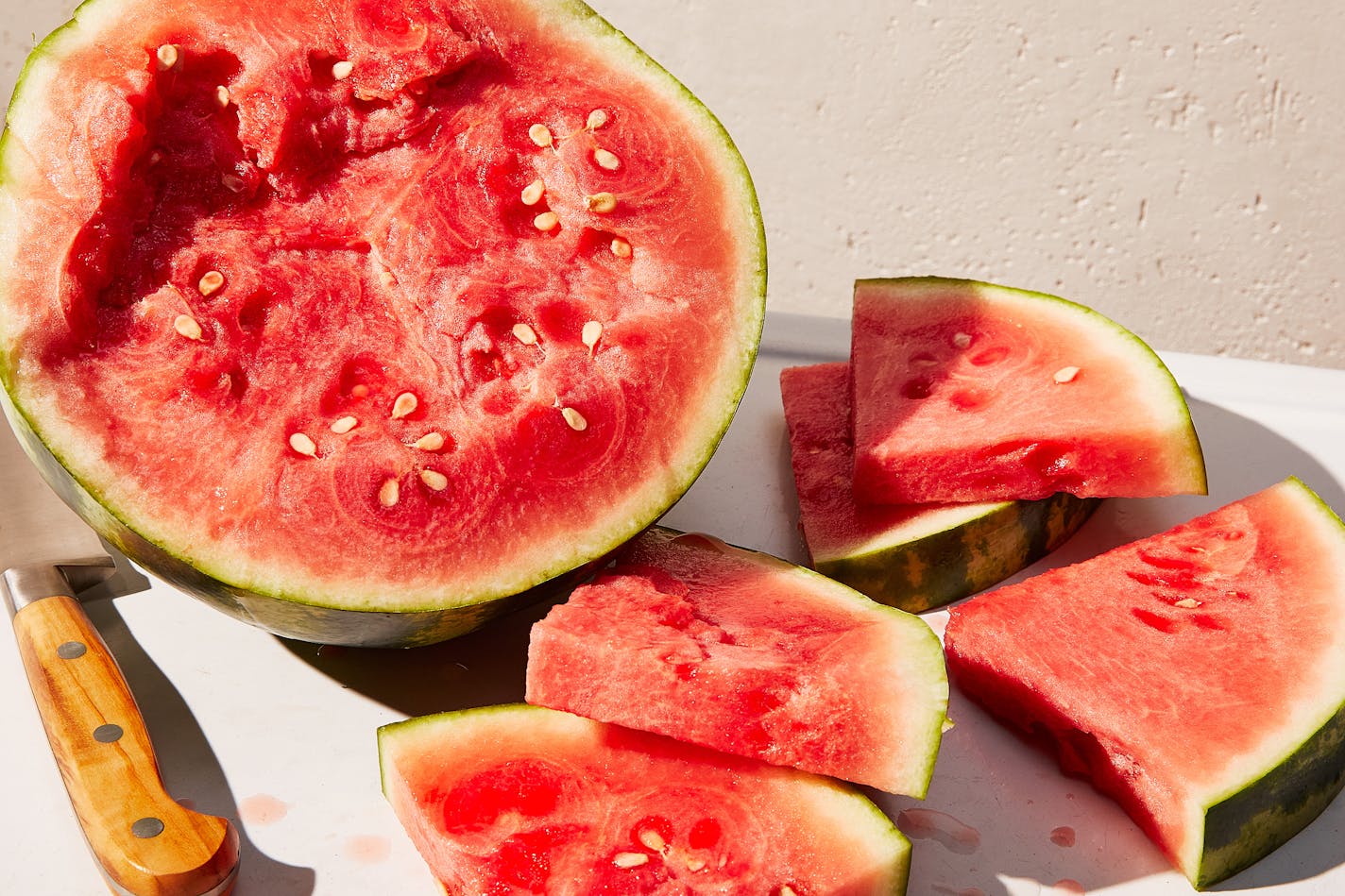 A whole watermelon cut up on a cutting board with a knife next to it.