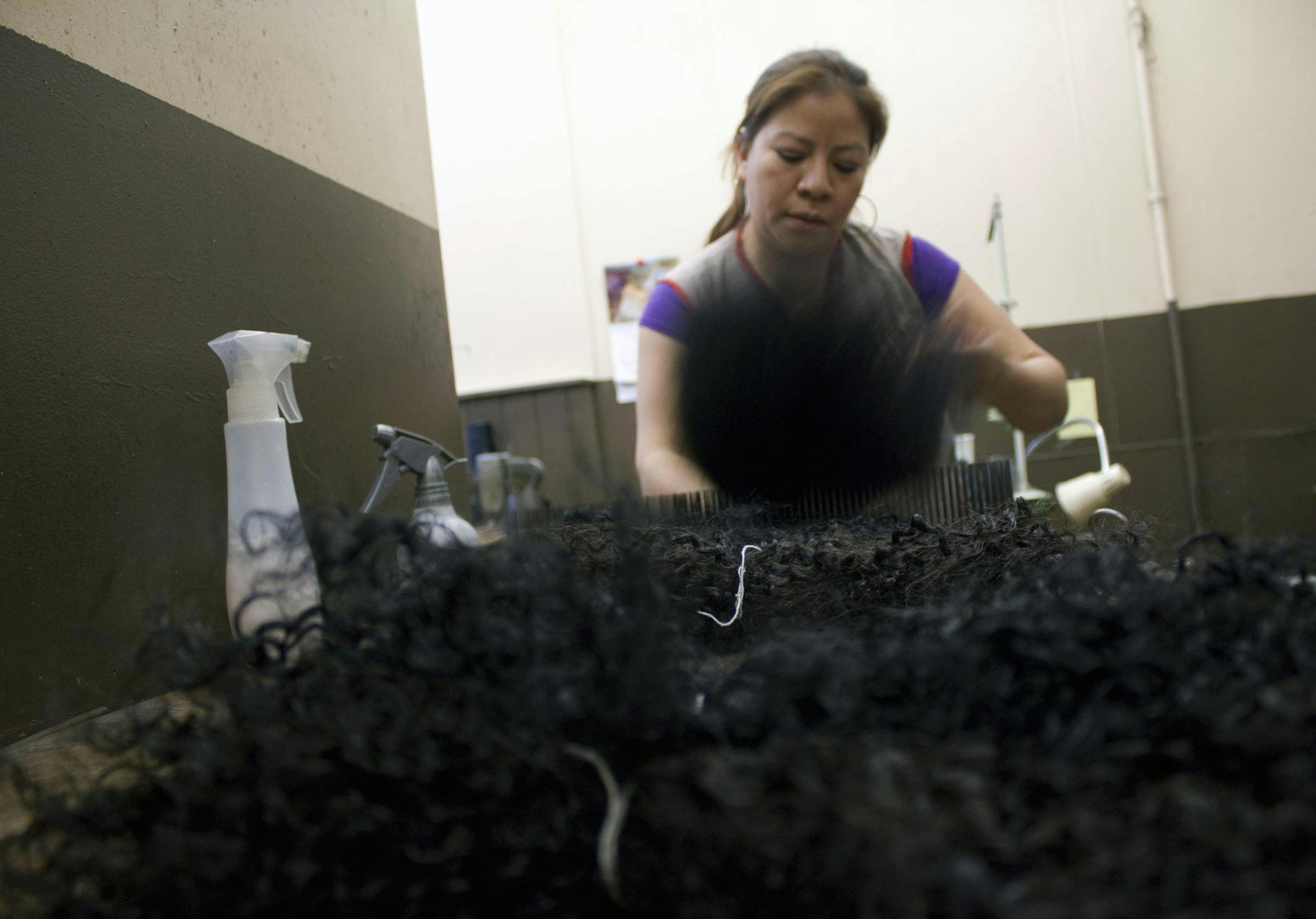 Marta Deleon combs bundles of human hair at Barbie's Hair World in Queens, New York, where she has processed raw hair for the past 18 years. (Columbia News Service/Adrienne Berard)