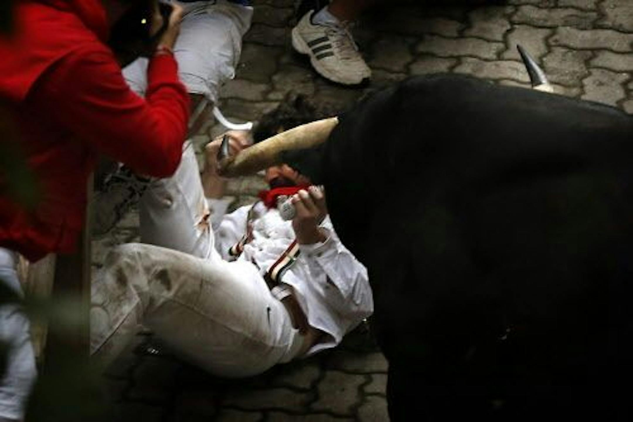 U.S. runner Bill Hillmann, 35, from Chicago lies on the ground after being gored on his right leg by a Victoriano del Rio ranch fighting bull during the running of the bulls of the San Fermin festival, in Pamplona, Spain, Wednesday, July 9, 2014.