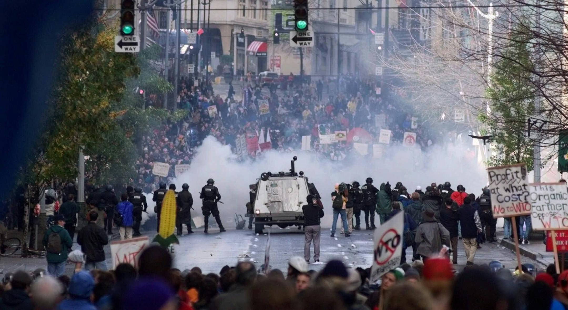 FILE - In this Nov. 30 1999, file photo, Seattle police use tear gas to push back World Trade Organization protesters in downtown Seattle. Saturday, Nov. 30, 2019 marks 20 years since tens of thousands of protesters converged on Seattle and disrupted a major meeting of the World Trade Organization. The protesters’ message was amplified not just by their vast numbers but by the response of overwhelmed police, who fired tear gas and plastic bullets and arrested nearly 600 people. Two decade