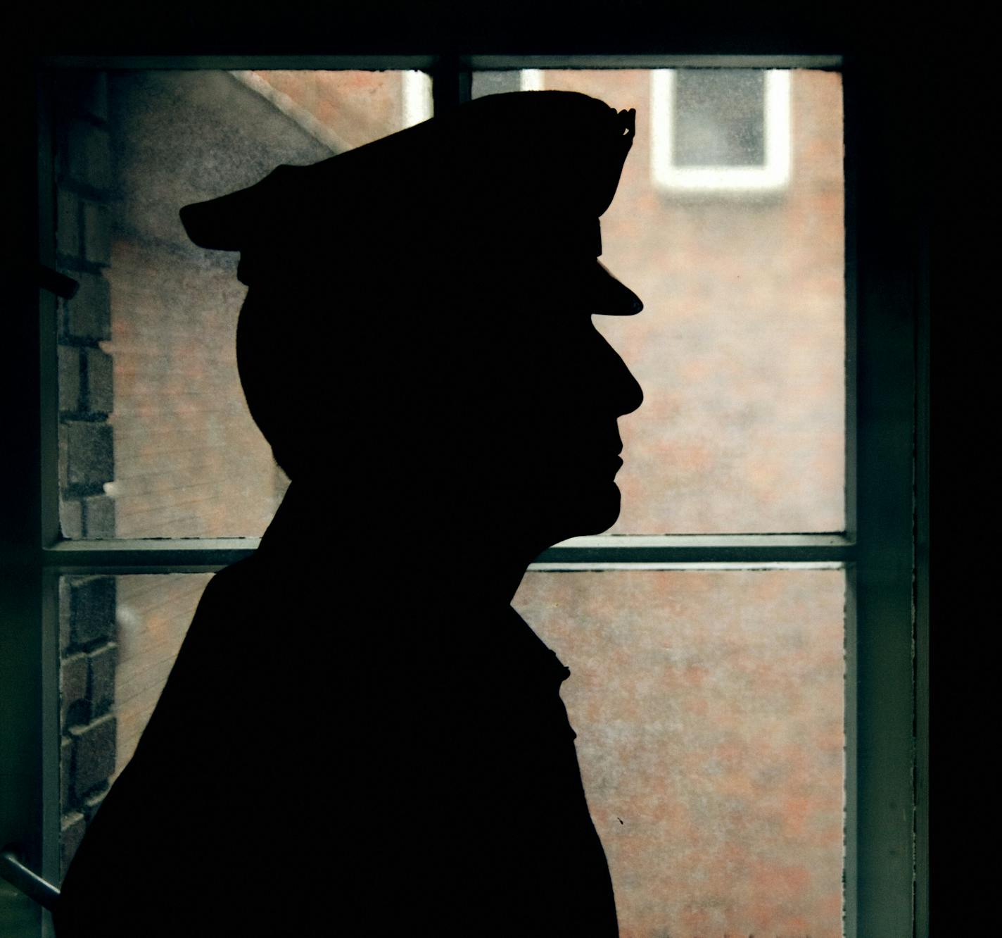 Warder's silhouette, prison walls outside the window.