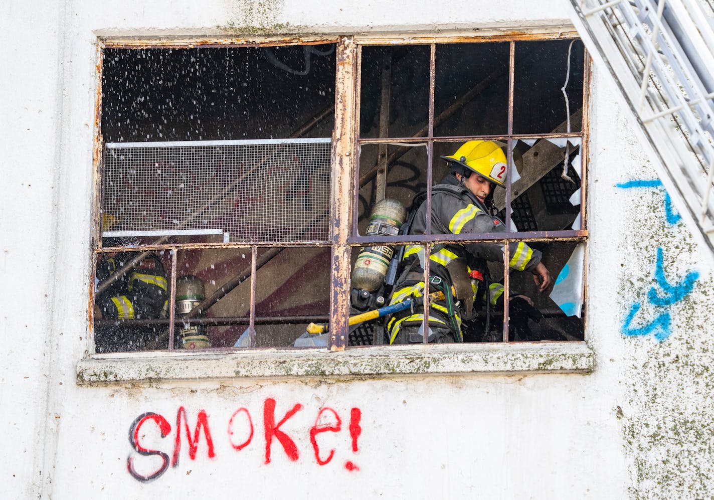 Firefighters, seen through windows, worked to put out a fire Wednesday in a grain elevator in south Minneapolis. Red graffiti on the building says "Smoke!"