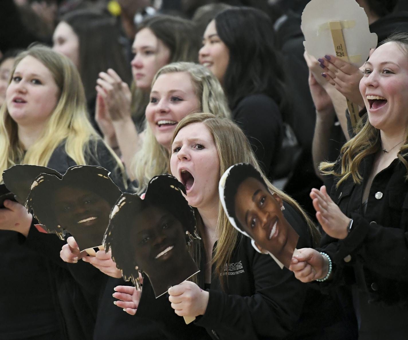 Grace Bailey, right of center, a senior at Austin, cheered for her team and held a cutout of Agwa Nywesh's face after Nywehs dunked the ball against Owatonna in the second half of Tuesday night's game. ] Aaron Lavinsky &#x2022; aaron.lavinsky@startribune.com Photos to accompany a feature on the ethnic diversification of Austin Minn., as seen through the Austin High School boys basketball and soccer programs, photographed Tuesday, Feb. 4, 2020.