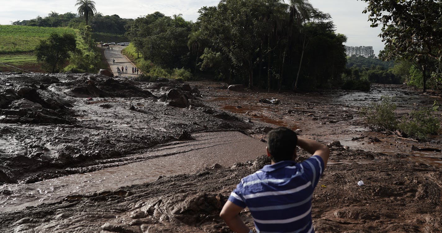 A man stands at a blocked road after a dam collapsed near Brumadinho, Brazil, Saturday, Jan. 26, 2019. The dam that held back mining waste collapsed, inundating a nearby community in reddish-brown sludge, killing at least seven people and leaving scores of others missing. (AP Photo/Leo Correa)