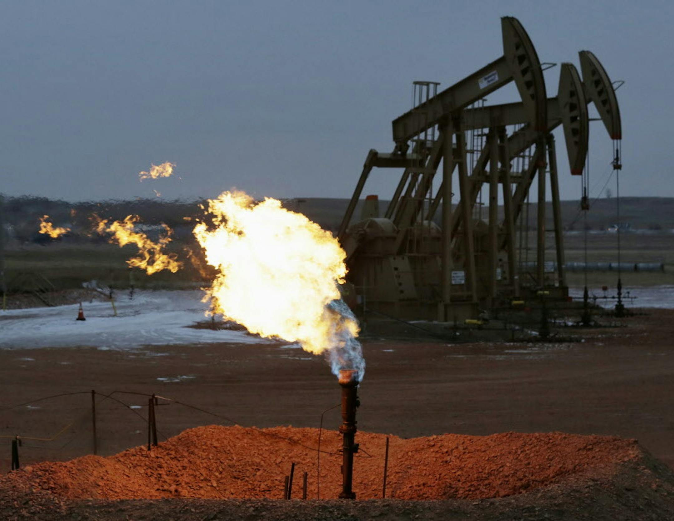 FILE - In this Dec. 17, 2014 file photo, oil pump jacks work behind a natural gas flare near Watford City, N.D. Iraqi and U.S. Energy Department officials toured western North Dakota this week to look at technologies the state is using to curb the wasteful burning of natural gas that's a byproduct of oil production. (AP Photo/Eric Gay, File)