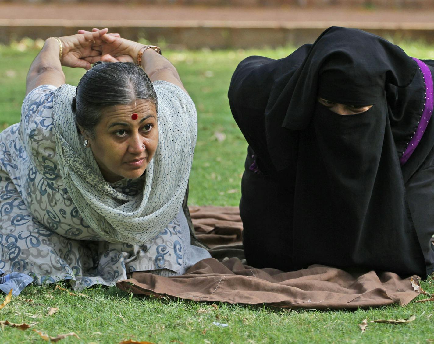 In this Sunday, June 14, 2015, photo, an Indian yoga trainer Chandrikaben Kansara, left teaches yoga to a Muslim woman in a garden in Ahmadabad, India. Yoga has a long history India, reaching back for thousands of years. The government of Prime Minister Narendra Modi has made clear it wants the first International Yoga Day, held on Sunday, June 21, 2015, to be taken seriously. (AP Photo/Ajit Solanki)