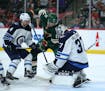 Wild left wing Marcus Foligno (17) tries to shove the puck between the pads of Winnipeg Jets goalie Connor Hellebuyck (37) while defended by Jets' Ben