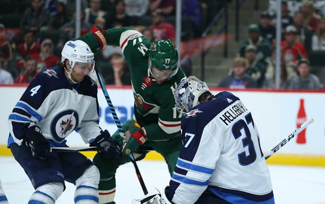 Wild left wing Marcus Foligno (17) tries to shove the puck between the pads of Winnipeg Jets goalie Connor Hellebuyck (37) while defended by Jets' Ben
