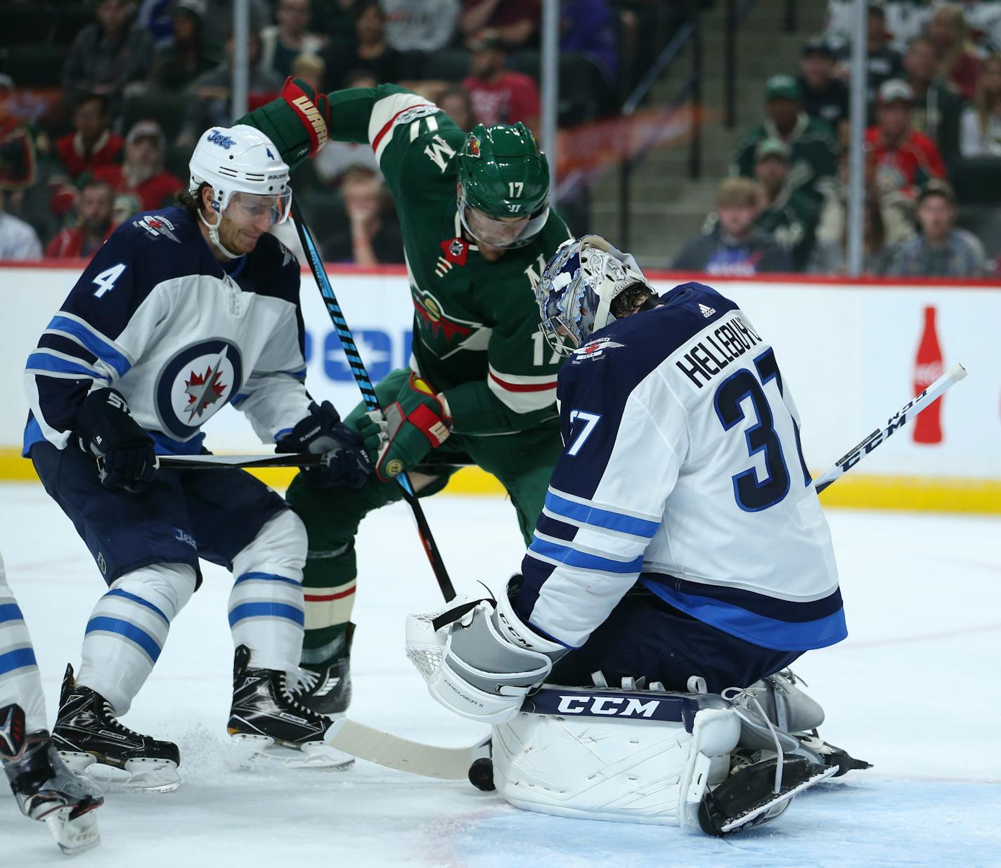 Wild left wing Marcus Foligno (17) tries to shove the puck between the pads of Winnipeg Jets goalie Connor Hellebuyck (37) while defended by Jets' Ben Chiarot (7).