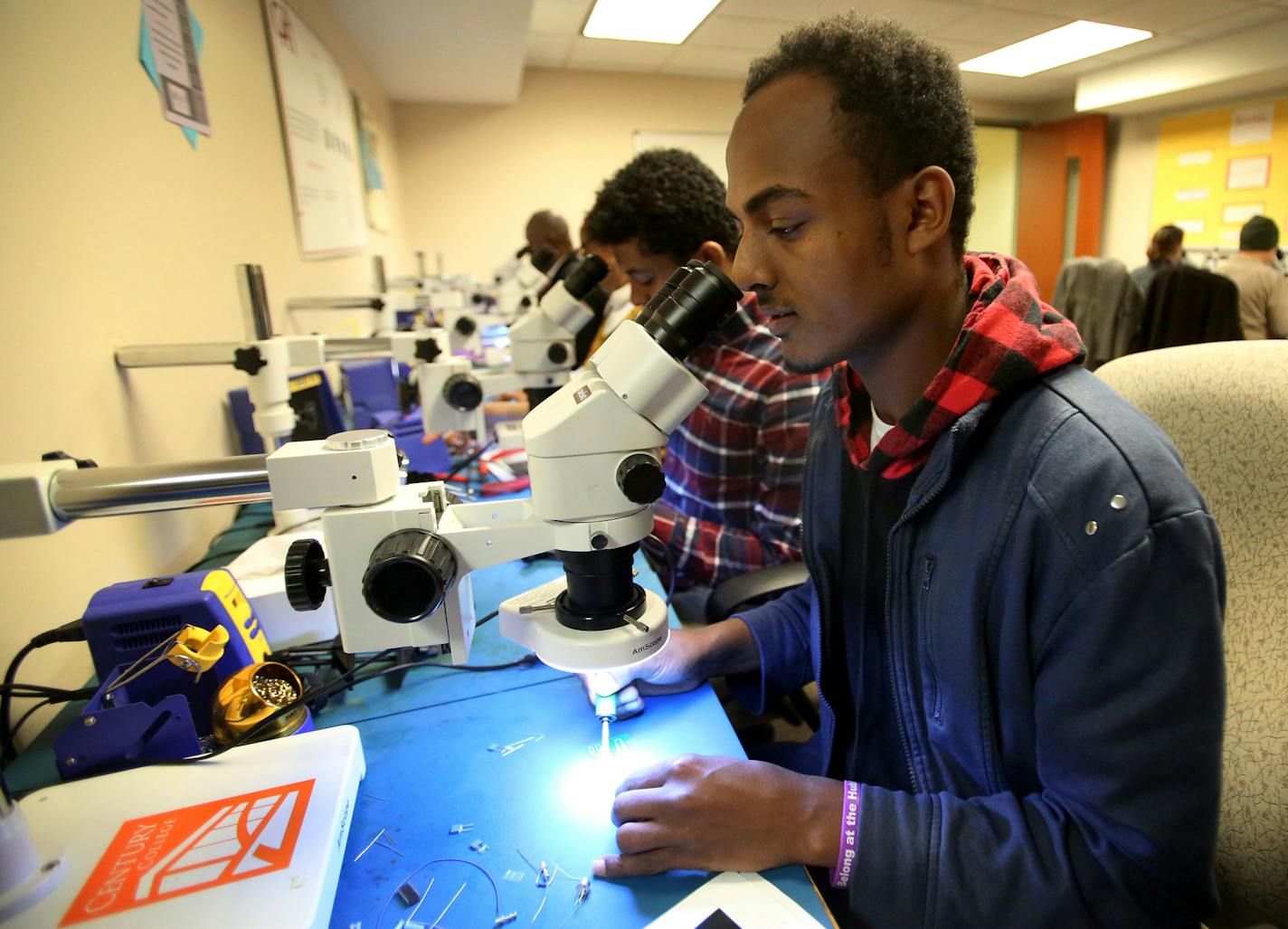 Immigrants and their relatives work on soldering electronic circuit boards during a 120-hour class that gets them certified for high-paying manufacturing jobs at CAPI in Minneapolis. Here, Dawit Gelata, originally from Ethiopia, looks through an industrial microscope while working on a circuit board.