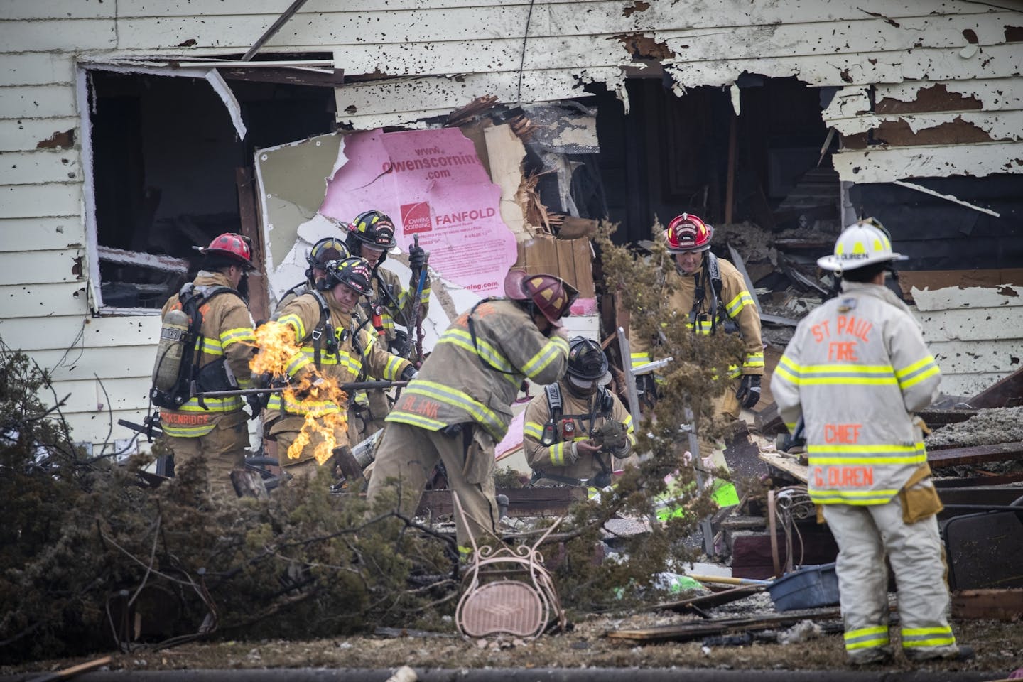 St. Paul firefighters work to clear brush away from a gas line still burning at the scene of a house explosion.