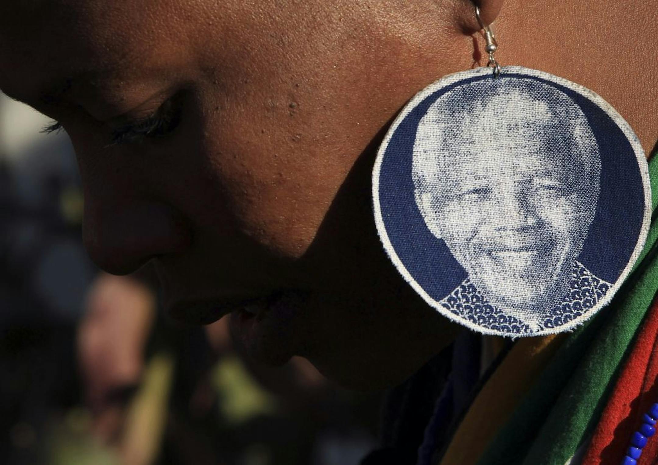 An unidentified woman wearing earrings bearing the image of former South African President Nelson Mandela, outside the Mediclinic Heart Hospital where he is being treated in Pretoria, South Africa, Wednesday, June 26, 2013. South Africa's president Jacob Zuma on Tuesday urged his compatriots to show their appreciation for Nelson Mandela, who is in critical condition in a hospital, by marking his 95th birthday next month with acts of goodness that honor the legacy of the anti-apartheid leader.