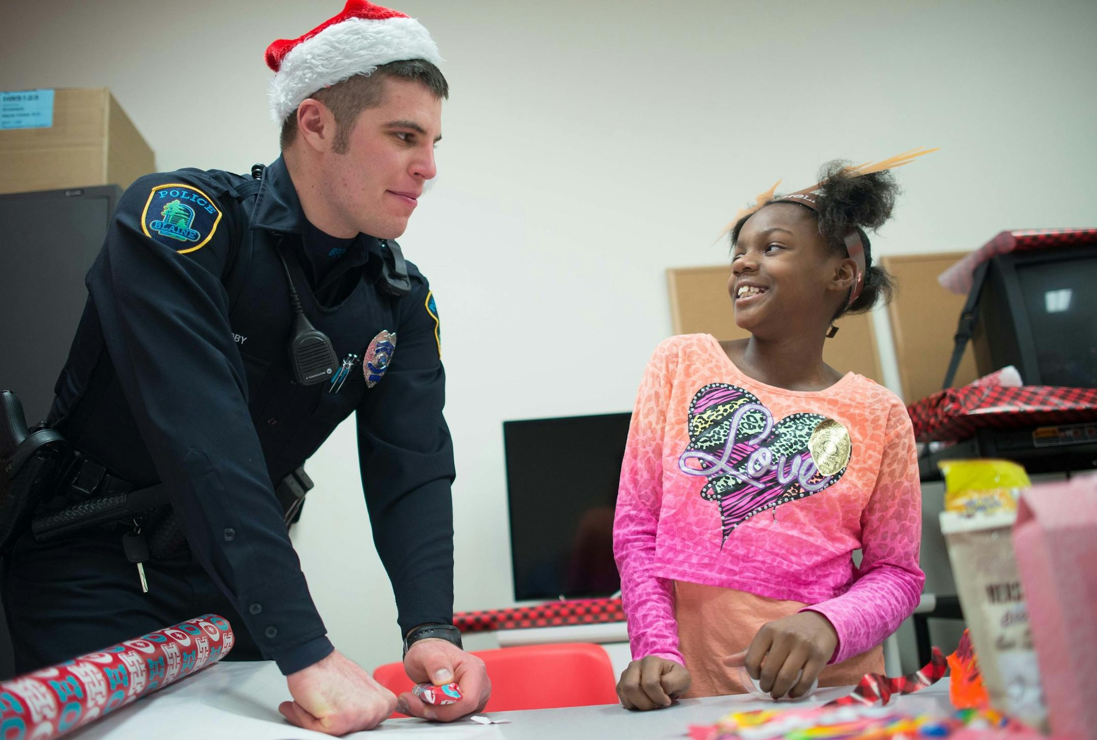 Blaine Police Officer Brad Nordby and 9-year-old Ra'Shauna McNeal, of University Elementary, share a laugh as they wrap gifts Tuesday night. ] AARON LAVINSKY • aaron.lavinsky@startribune.com Anoka County cops and firefighters conduct their annual Heroes and Helpers event Tuesday, Dec. 2, 2014 at Target in Blaine. 48 children were given $100 gift cards to spend on themselves and their families while being escorted around target by first responders.