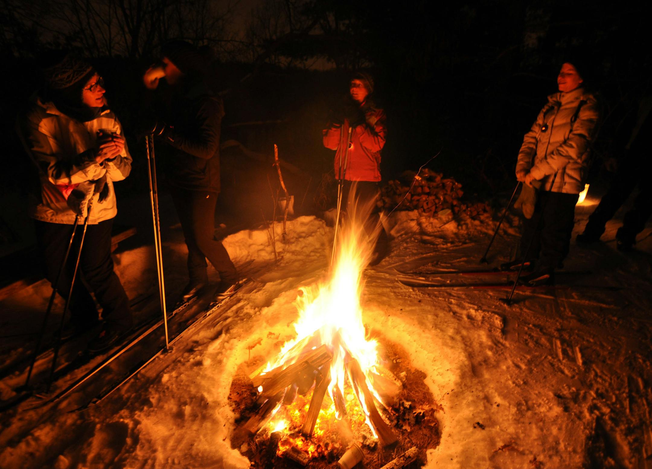 Photo by Liz Rolfsmeier Edie Stone and Laina Rominski (of Lakeville), Candi Arries (of St. Louis Park), and Marnie Douangmala (of West St. Paul) warm up around a fire during the Trails by Candlelight event at Lebanon Hills.