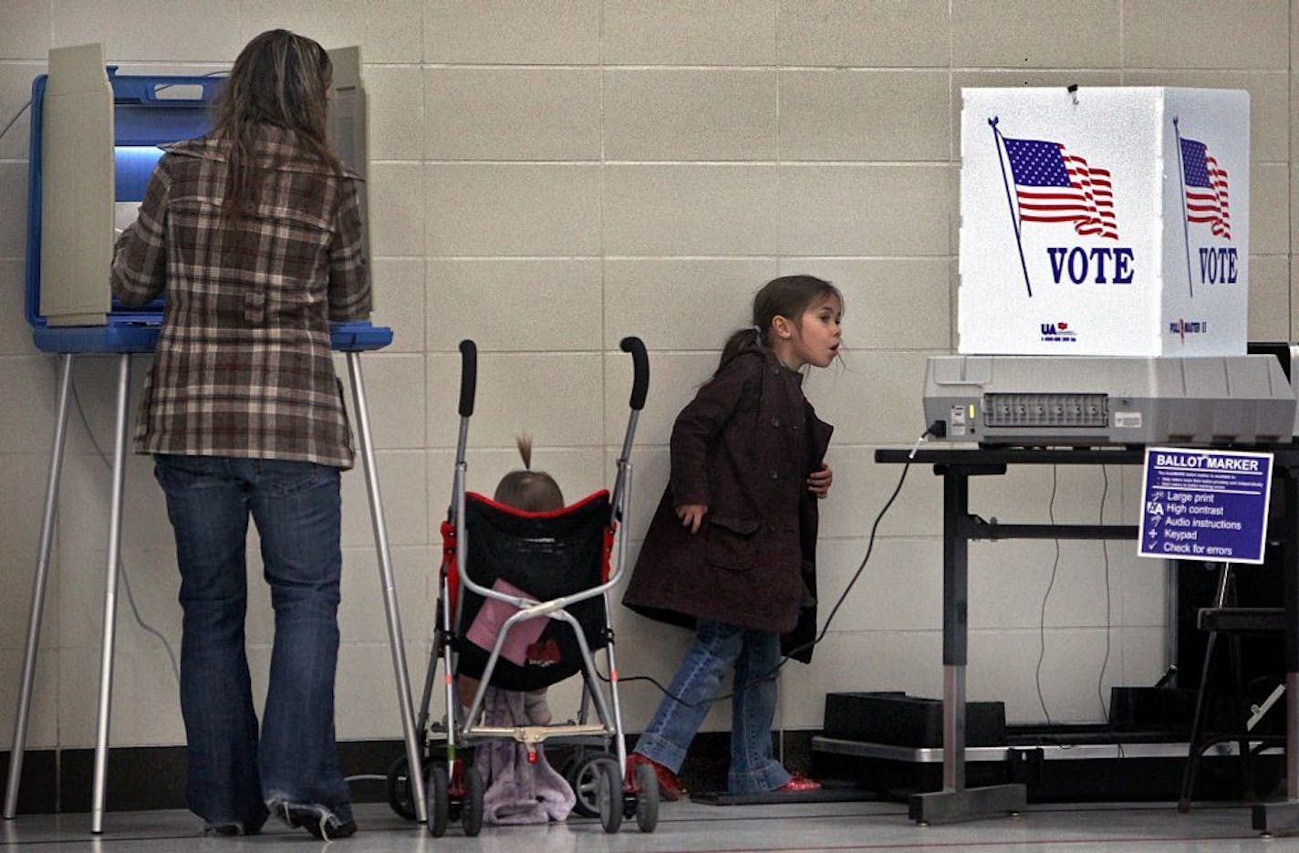 Abigail Thomes, almost six years old, explored the polling place at Wilson Elementary School in Anoka, while her mother, Melissa Thomes, filled out her ballot. Macy, 15 months, is in the stroller. Melissa explained, "It's important to vote, because I have two in school and I want the schools to have appropriate funding."