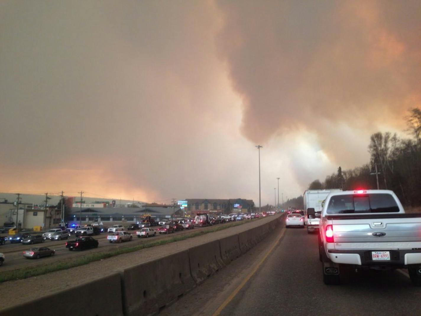 Smoke from a wildfire rises in the air as cars line up on a road in Fort McMurray, Alberta, Tuesday, May 3, 2016. At least half of a northern Alberta city was ordered evacuated Tuesday as a wildfire whipped by winds engulfed homes and sent ash raining down on residents.