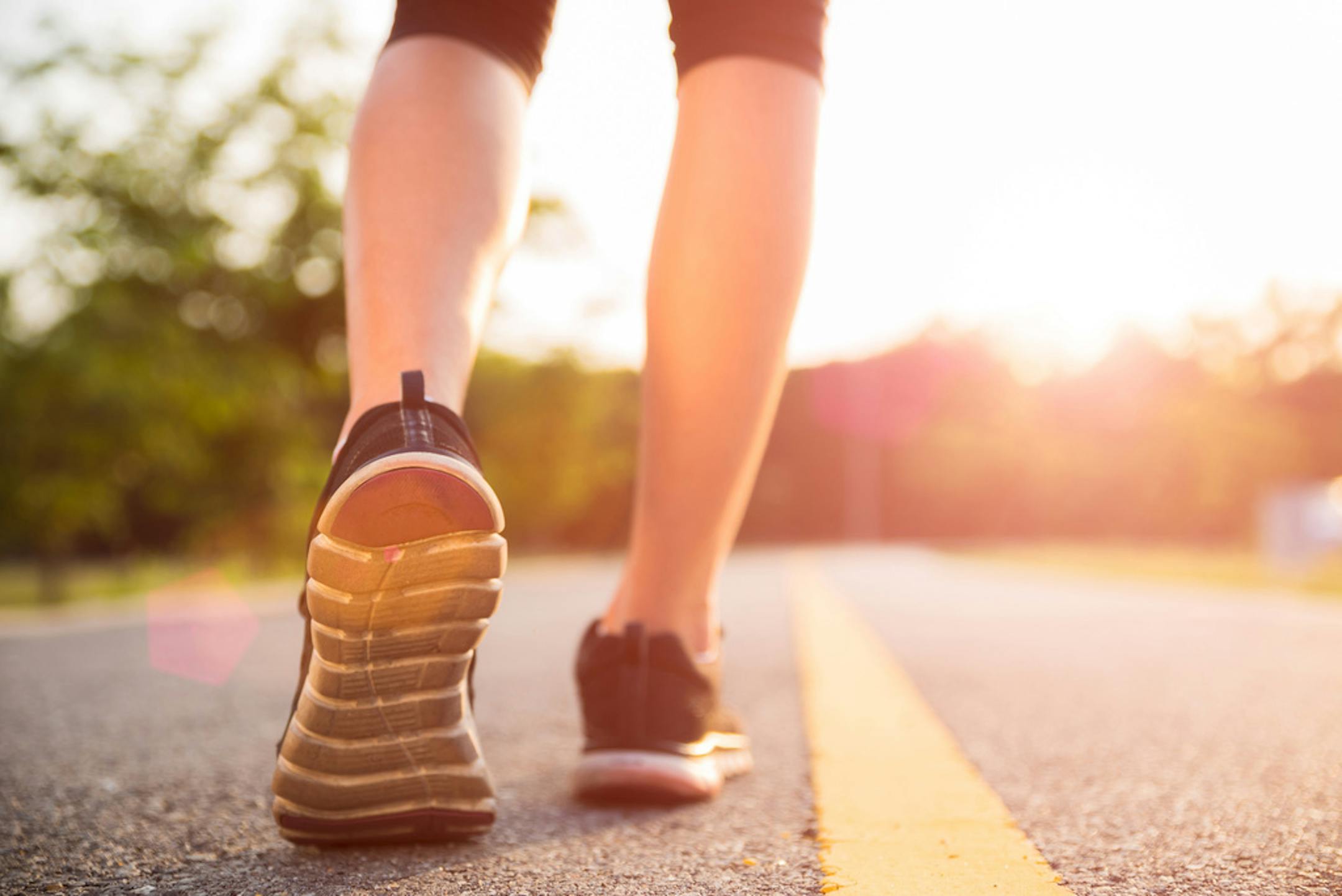 Person walking on roadway, seen from knee down, wearing cropped leggings and tennis shoes.