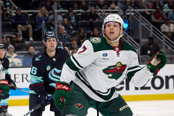 Minnesota Wild defenseman Brock Faber (7) and Seattle Kraken right wing Kailer Yamamoto (56) look to the stands to see where a puck landed during the 