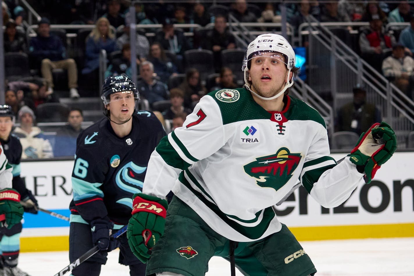 Minnesota Wild defenseman Brock Faber (7) and Seattle Kraken right wing Kailer Yamamoto (56) look to the stands to see where a puck landed during the third period of an NHL hockey game, Sunday, Dec. 10, 2023, in Seattle. The Wild won 3-0. (AP Photo/John Froschauer)