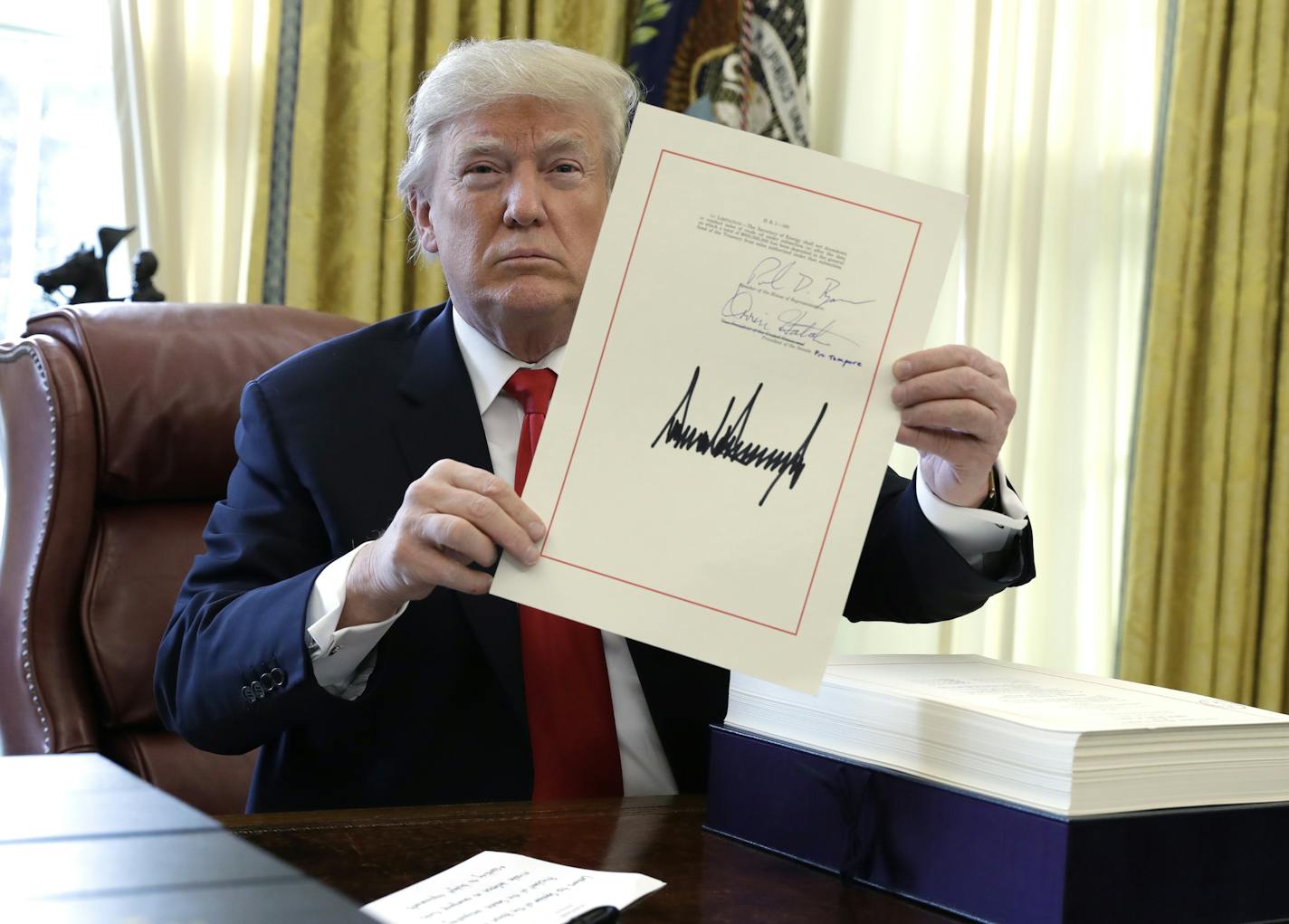 President Donald Trump displays the $1.5 trillion tax overhaul package he had just signed, Friday, Dec. 22, 2017, in the Oval Office of the White House in Washington. Trump touted the size of the tax cut, declaring to reporters in the Oval Office before he signed it Friday that "the numbers will speak." (AP Photo/Evan Vucci)