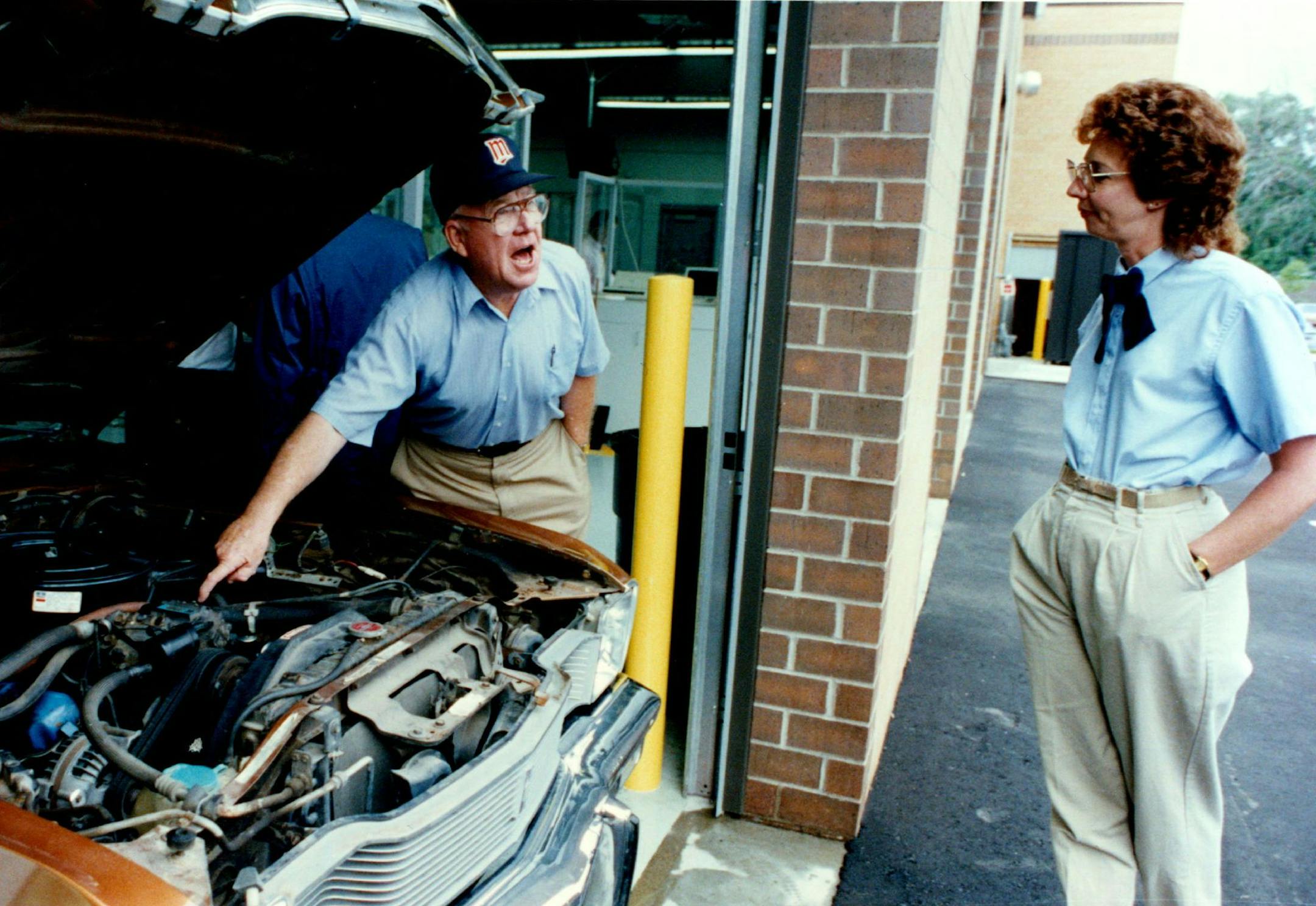 July 1, 1991 First day of mandatory inspection of vehicle emissions at Hiawatha station, 3435 Hiawatha Av., Minneapolis. "That thing cost me 118 bucks," said James Danaher as he talked about some new car parts with Peggy Vincent, from Maryland, who was in town to help with the launching of the inspection stations. July 2, 1991 Charles Bjorgen, Minneapolis Star Tribune