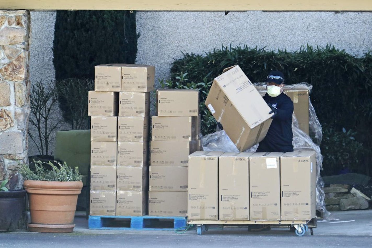 A worker at the Life Care Center in Kirkland, Wash., wears a mask as he stacks newly arrived boxes of gloves, gowns, and other protective gear on a cart, Monday, March 9, 2020, near Seattle. The nursing home is at the center of the outbreak of the new coronavirus in Washington state.