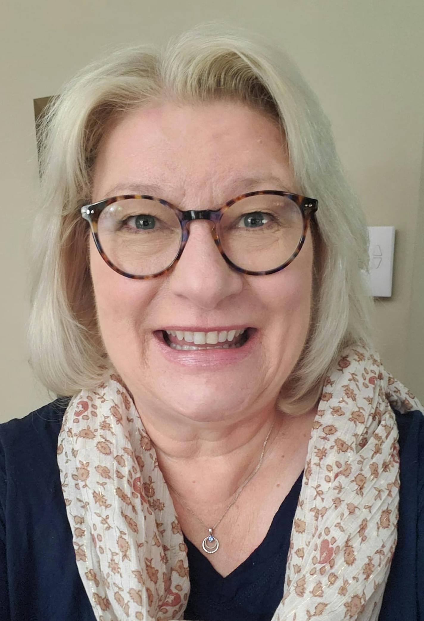 Headshot of a woman wearing glasses and a floral scarf over a black V-neck top.