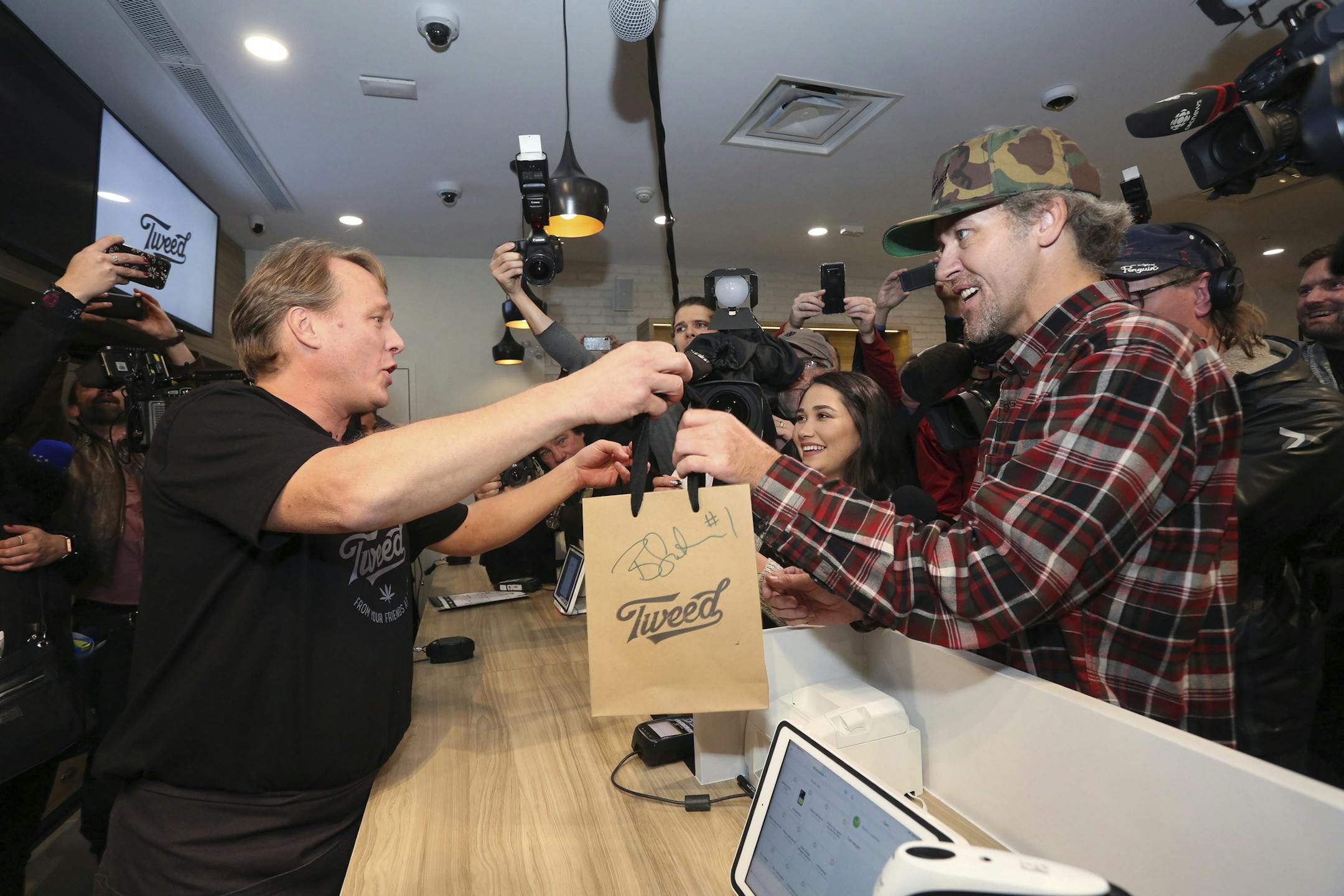 Bruce Linton, left, in a file photo from Oct. 17, 2018 , passes a bag with the first legal cannabis for recreation use sold in Canada. (Paul Daly/The Canadian Press via AP) ORG XMIT: MIN2018101700000157