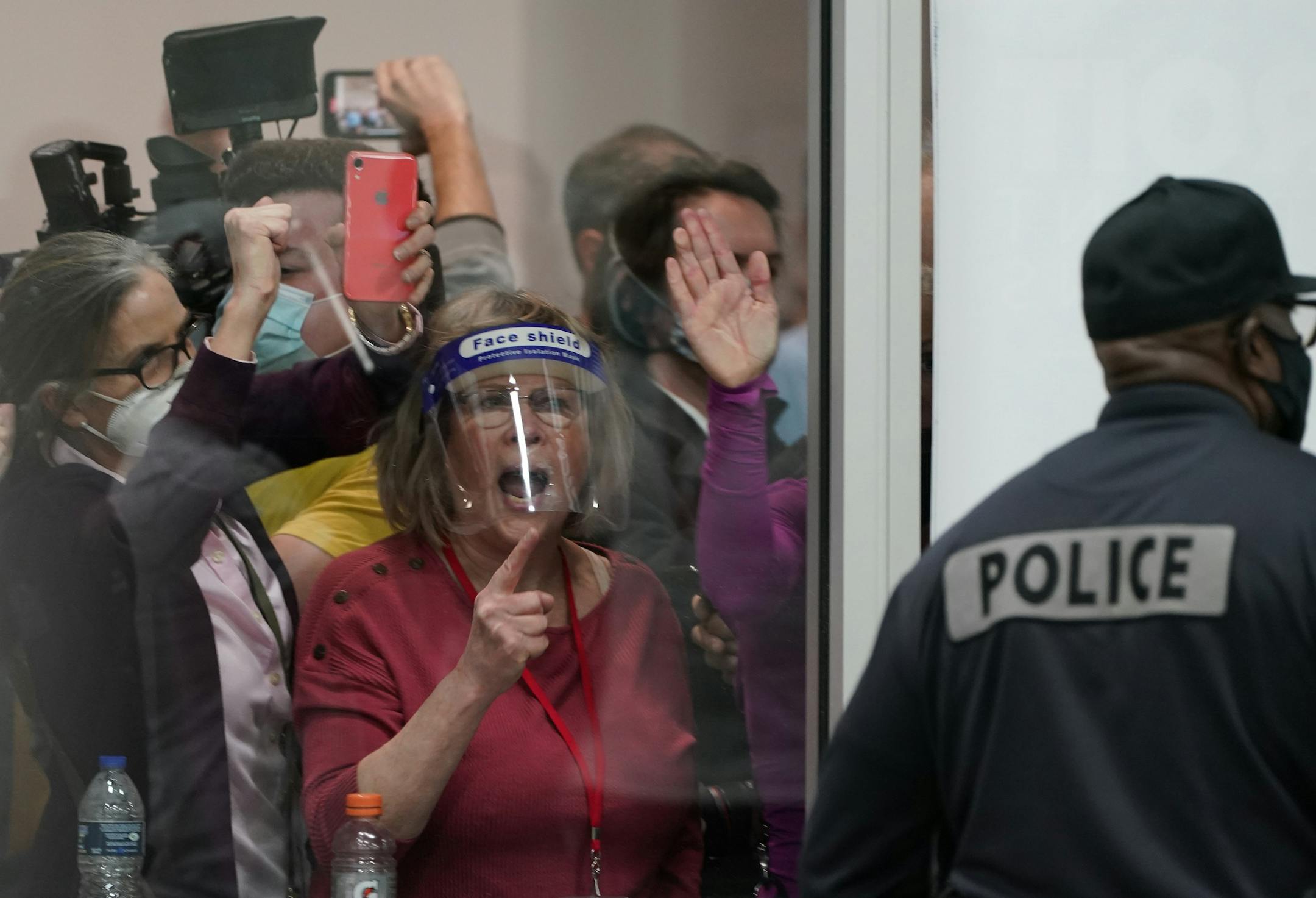 Election challengers yell as they look through the windows of the central counting board as police were helping to keep additional challengers from entering due to overcrowding, Wednesday, Nov. 4, 2020, in Detroit.