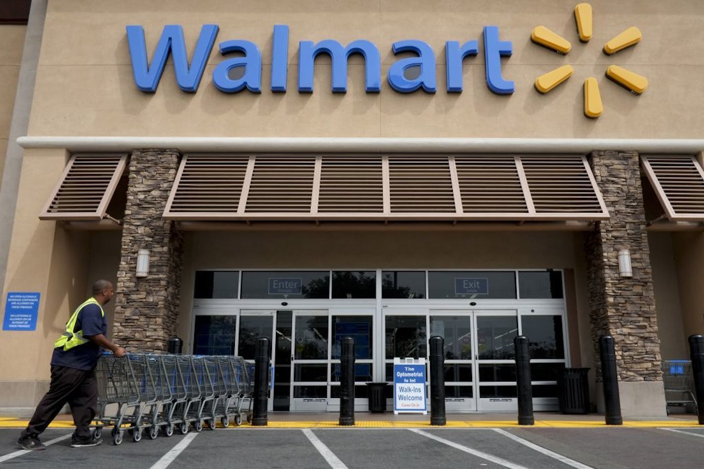 FILE - In this May 9, 2013 file photo, a worker pushes shopping carts in front of a Wal-Mart store in La Habra, Calif. The world's largest retailer plans to work with DirectHealth.com, an online health insurance comparison site and agency, to allow shoppers to compare coverage options and enroll in Medicare plans or the public exchange plans created under the Affordable Care Act.