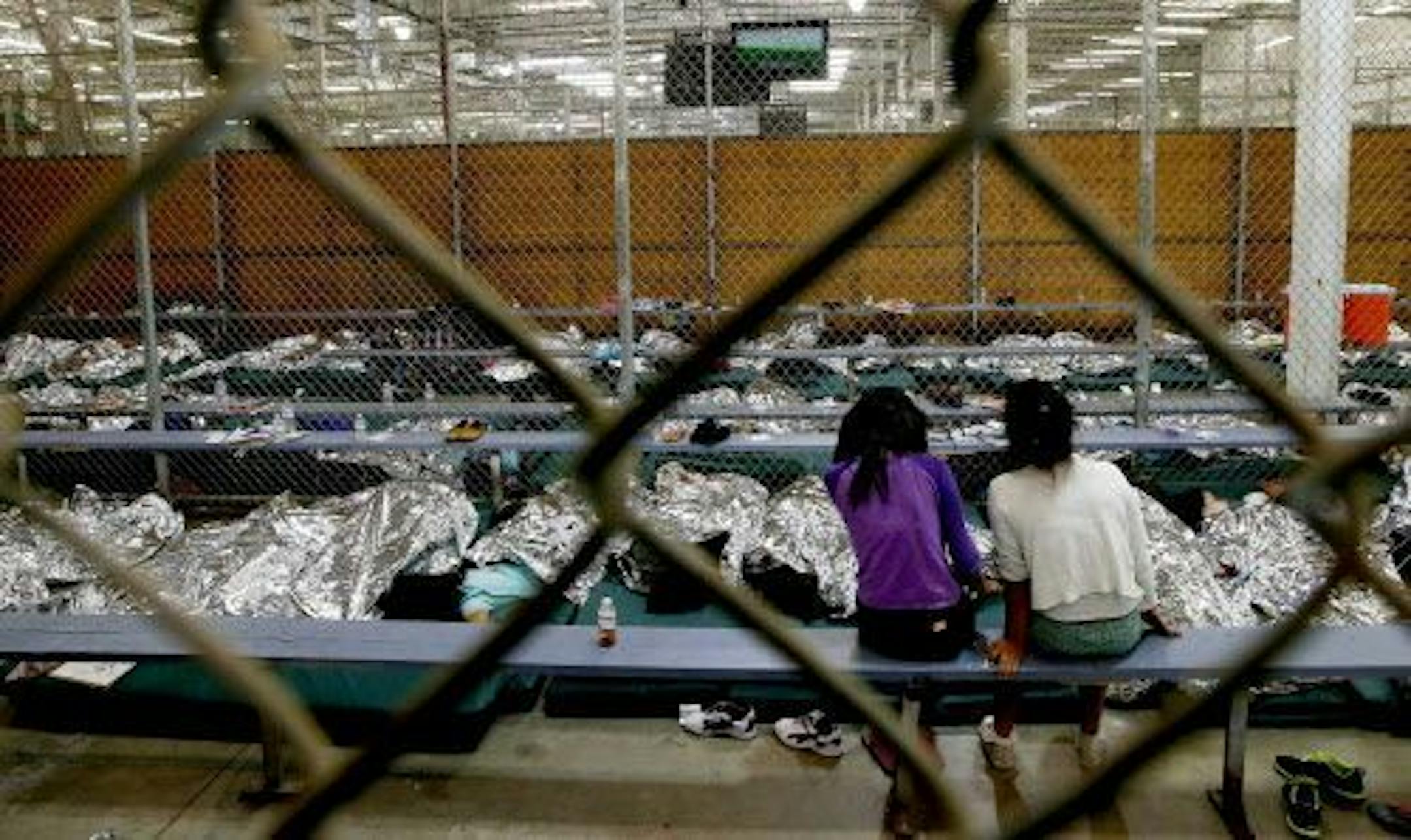 Two young girls watch a World Cup soccer match on a television from their holding area where hundreds of mostly Central American immigrant children are being processed and held at the U.S. Customs and Border Protection Nogales Placement Center on Wednesday, June 18, 2014, in Nogales, Ariz.