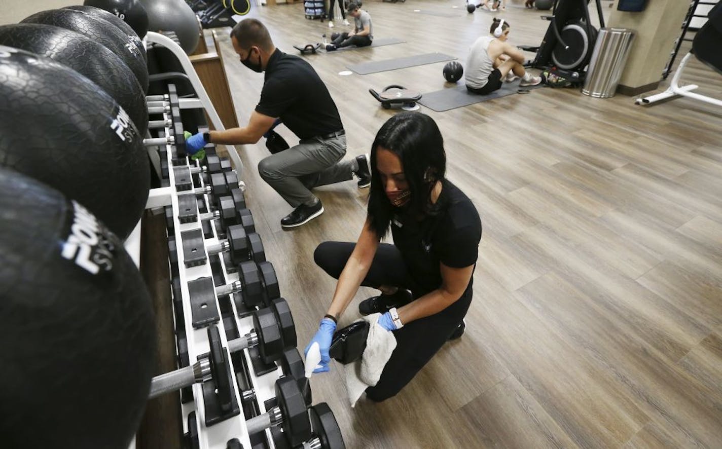 Jason Nichols, left, facilities operation manager at Life Time, and Jennifer McKeon, right, facilities operations national manager at Life Time, disinfect hand weights at a Phoenix Life Time.