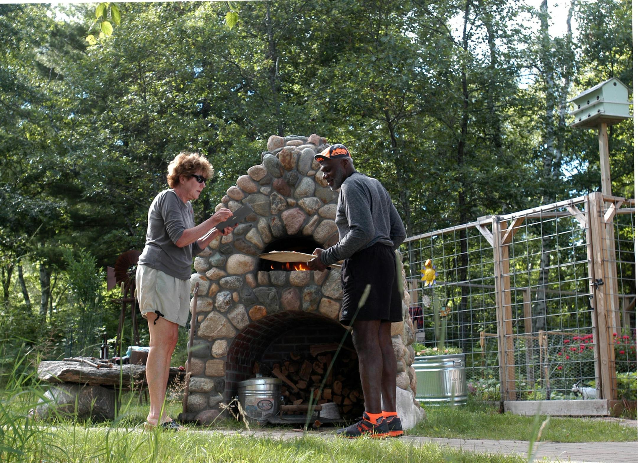 Diane and Alan Page bake pizzas in their outdoor pizza stone oven. Diane is taking a picture of the fresh pizza out of the oven.