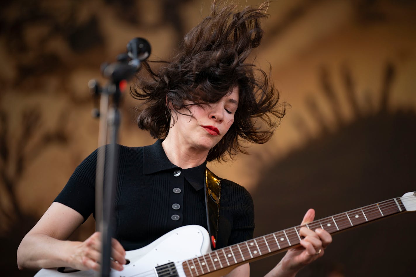 Guitarist Carrie Brownstein of Sleater-Kinney is performing outdoors and her dark brown hair is blowing in the wind.