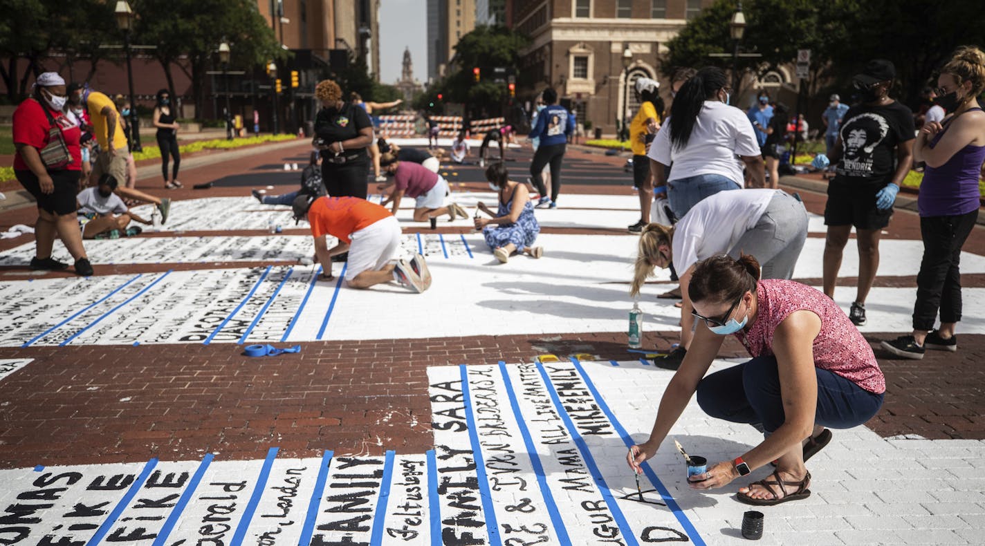 People signed their names on the words of the END RACISM NOW mural that is painted along Main Street, Saturday, June 27, 2020, in downtown Fort Worth, Texas. Deborah Peoples, right, who organized for the anti-racism message, said "we should be involved in the dialogue of how to end systemic racism." (Yffy Yossifor/Star-Telegram via AP)